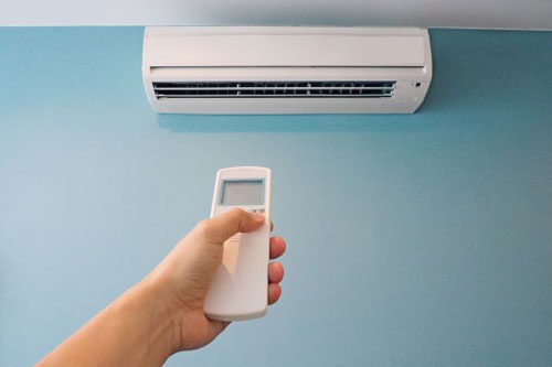 A hand holding a remote control under a unit of air conditioner 